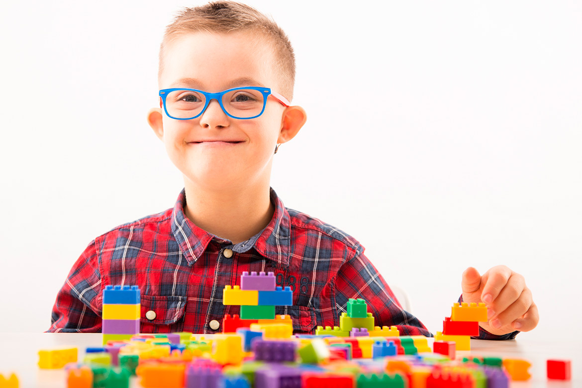 A boy with glasses and a red shirt is absorbed in playing with Legos, demonstrating imaginative play and fine motor skills.