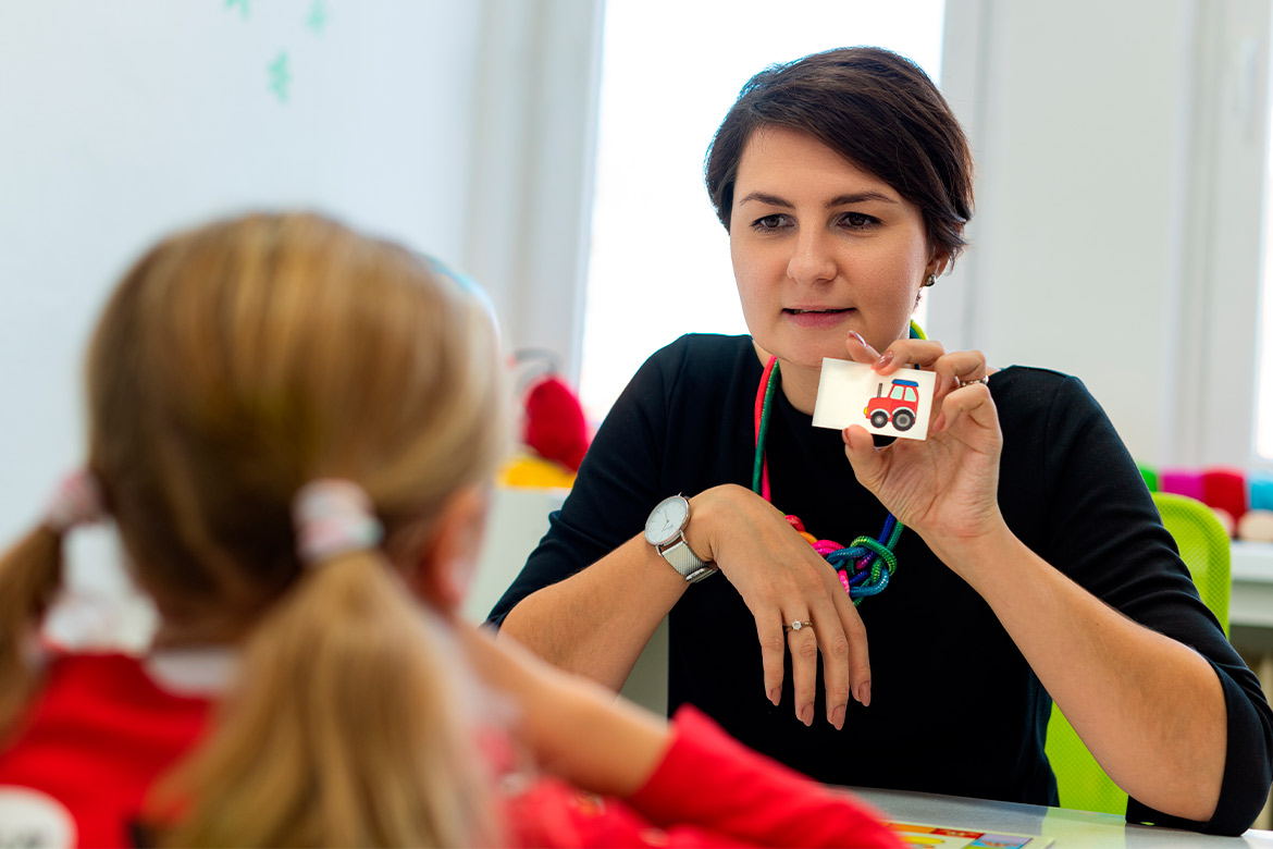 A woman holds a card with a sticker, symbolizing cognitive skill enhancement in occupational therapy for young minds.