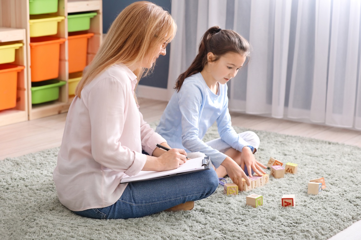 A woman and a young girl sit on the floor, engaged in play with colorful building blocks, fostering creativity and learning. Occupational Therapy services