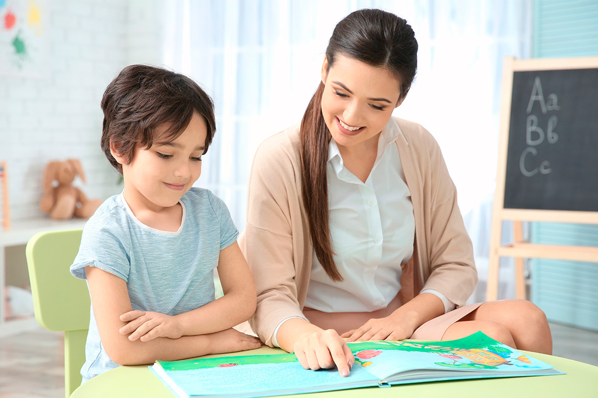 A young child reading a book with a woman, part of a speech therapy activity, showing joy and concentration.