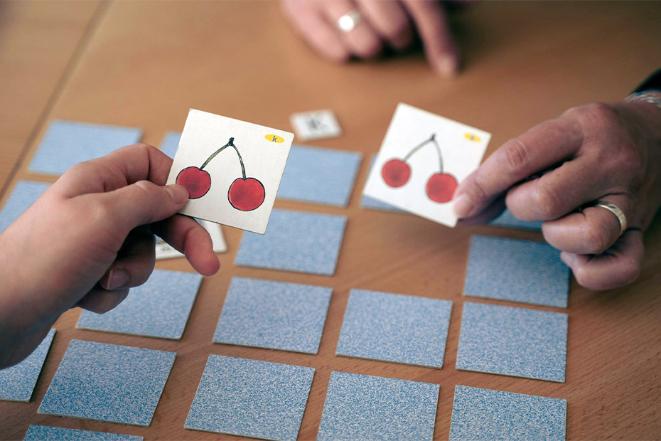 Two people engaged in a card game featuring cherries, promoting speech therapy skills for children.