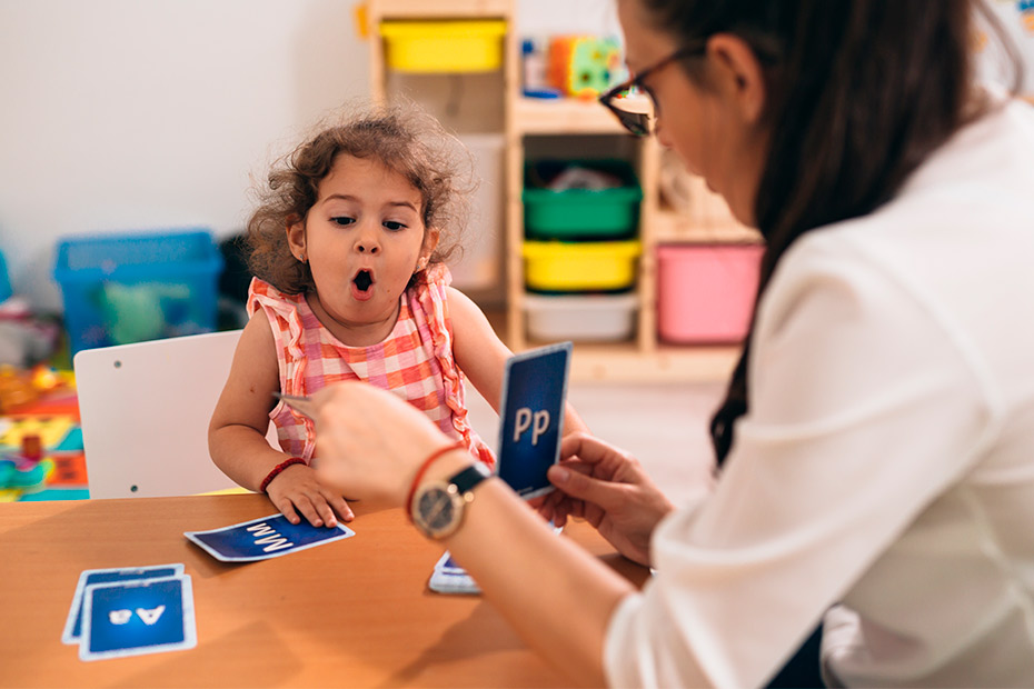 A woman engages in playful activities with a child in a classroom setting, focusing on speech therapy games.