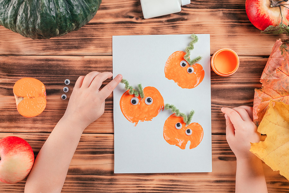 A child's hand displays a pumpkin craft on a table, showcasing a creative activity for occupational therapy at home.