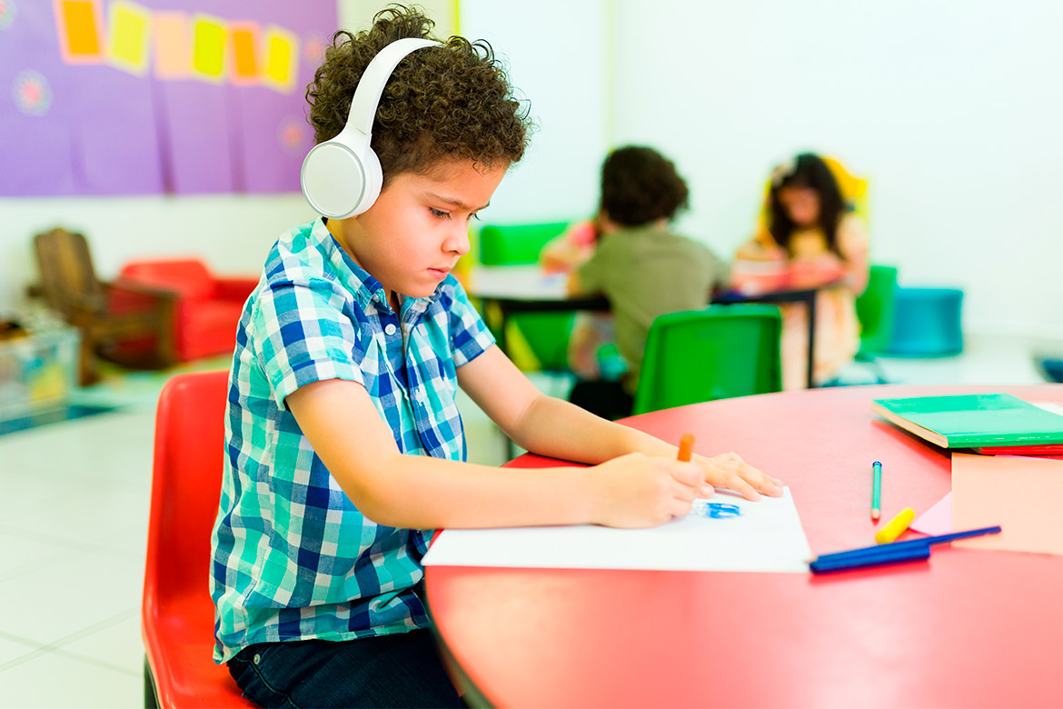 A young boy wearing headphones sits at a table, engaged in an activity related to occupational therapy for autism.
