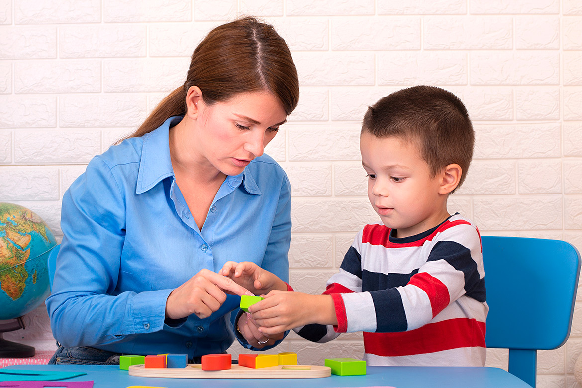 A woman assists a young boy with a puzzle, highlighting the importance of support in child development and therapy needs.
