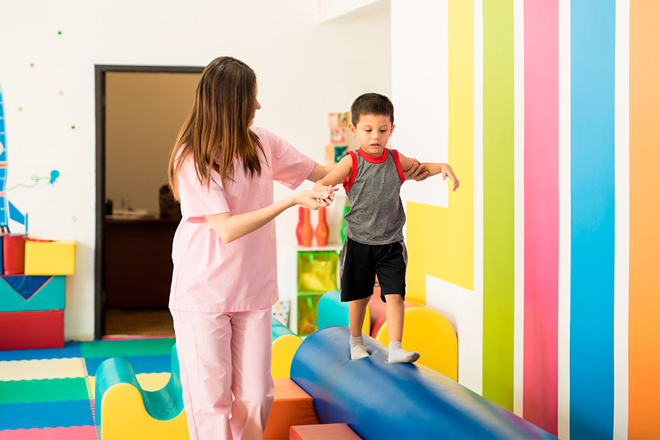 A woman assists a child on a vibrant play mat, illustrating engagement in developmental activities for potential therapy needs.