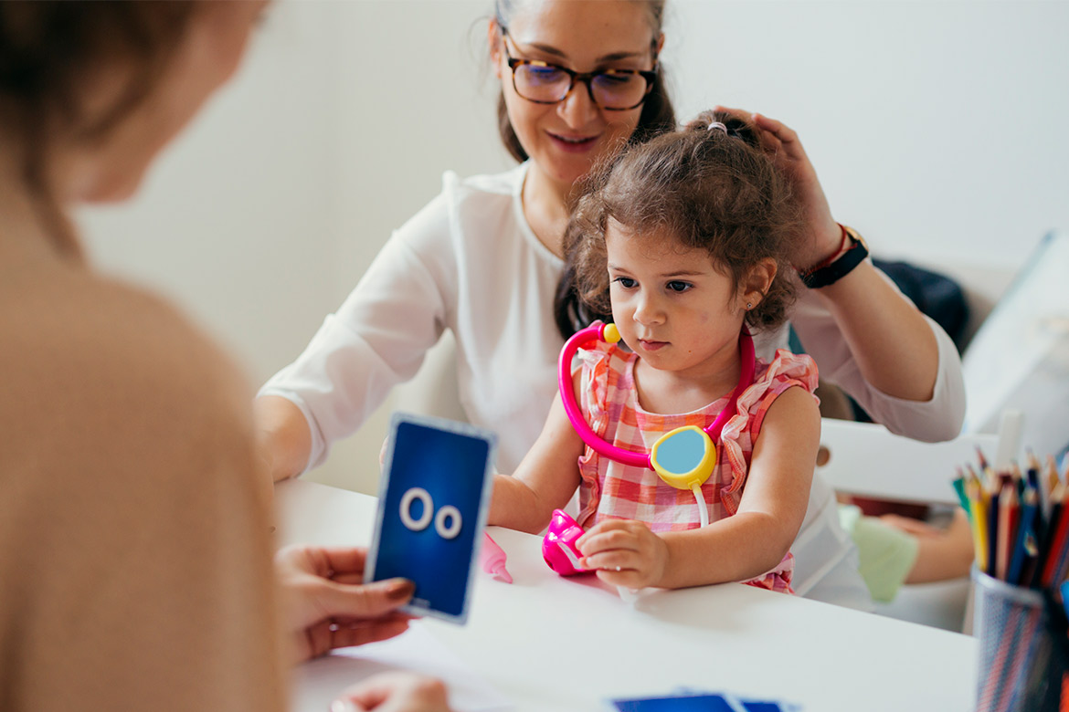 A woman and a child are seated at a table, focused on a card related to speech therapy in McAllen, TX.