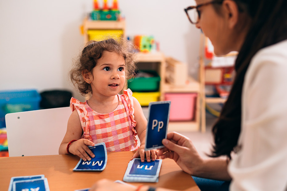 A woman and child engaged in a card game in a classroom setting, promoting interactive learning and communication skills.