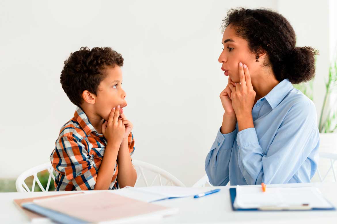 Speech Therapy Session. Woman working on kid boy pronunciation sitting at desk indoors. Professional speech therapist lady helping little patient with stuttering issue. Logopedic correction
