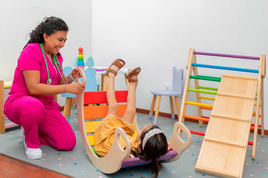 Latina pediatric doctor, laughing while playing with a girl in the play area of her office