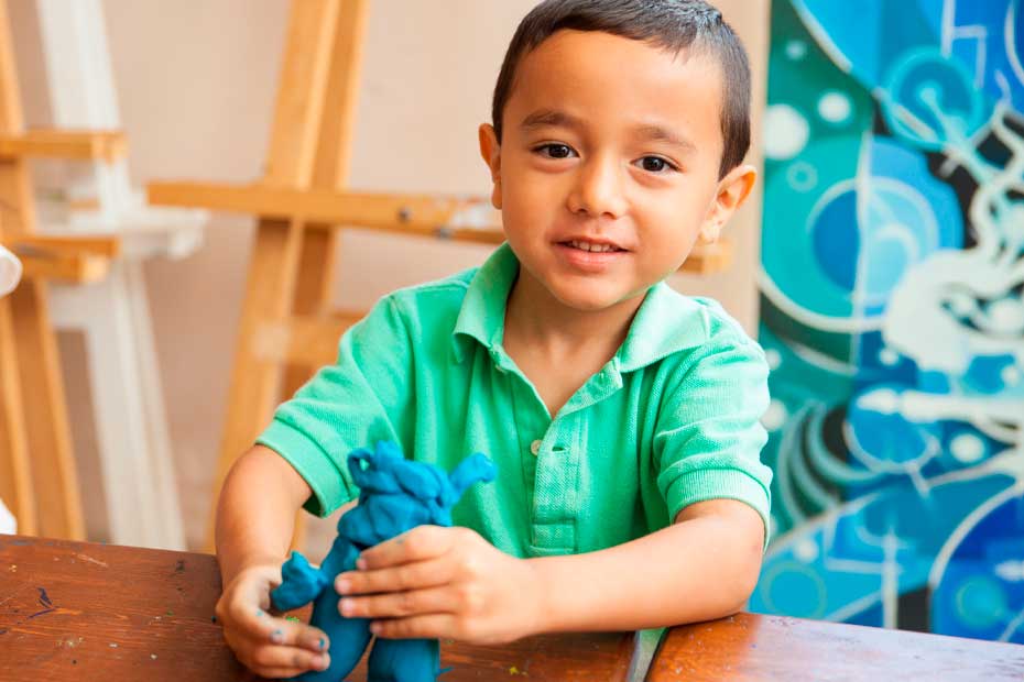Portrait of a little boy using clay to make a figure during his art and sculpture class