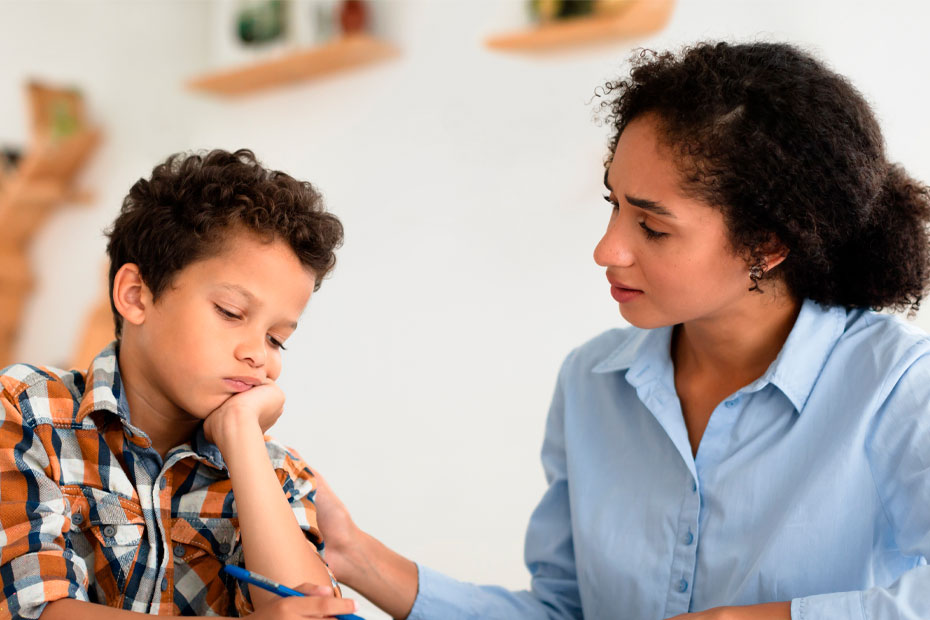 Kid School Learning Problems. Mom Comforting And Supporting Unhappy Schoolboy Son While He Having Hard Time With Homework Sitting At Desk Indoors. Child Suffering Having Educational Issue