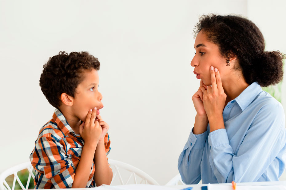 Speech Therapy Session. Woman working on kid boy pronunciation sitting at desk indoors. Professional speech therapist lady helping little patient with stuttering issue. Logopedic correction