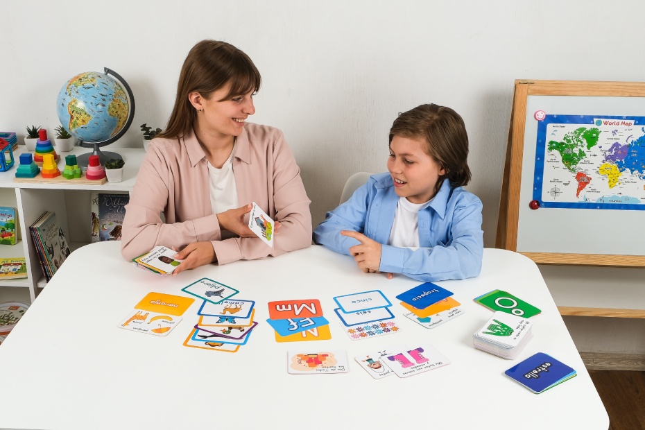 Happy teacher and young boy learning Spanish together with flashcards in a bilingual classroom. Concept of language development, communication, and fun education for kids.
